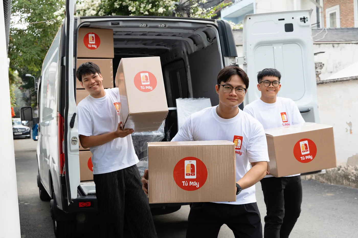Three Tủ Mây crew carrying boxes from the open van on a Ho Chi Minh City street