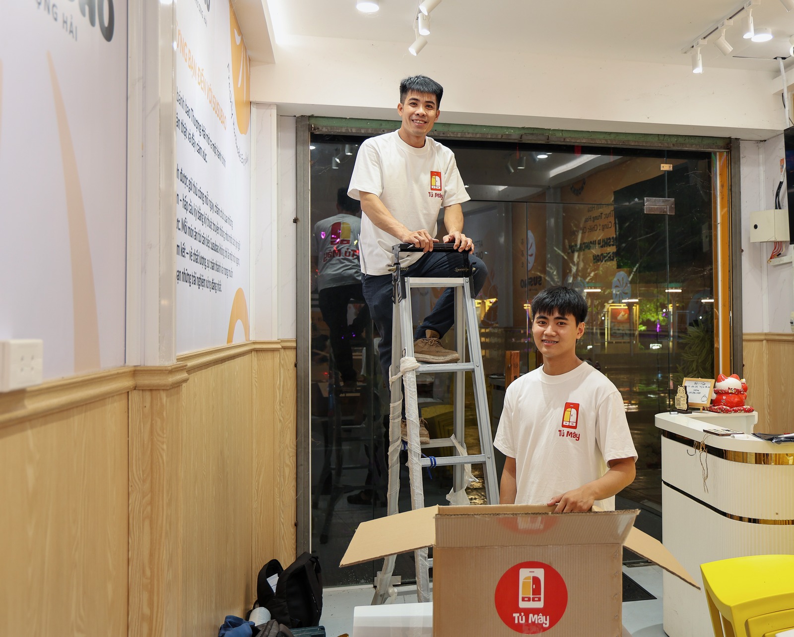 Two Tủ Mây crew members with a ladder and a box in the restaurant