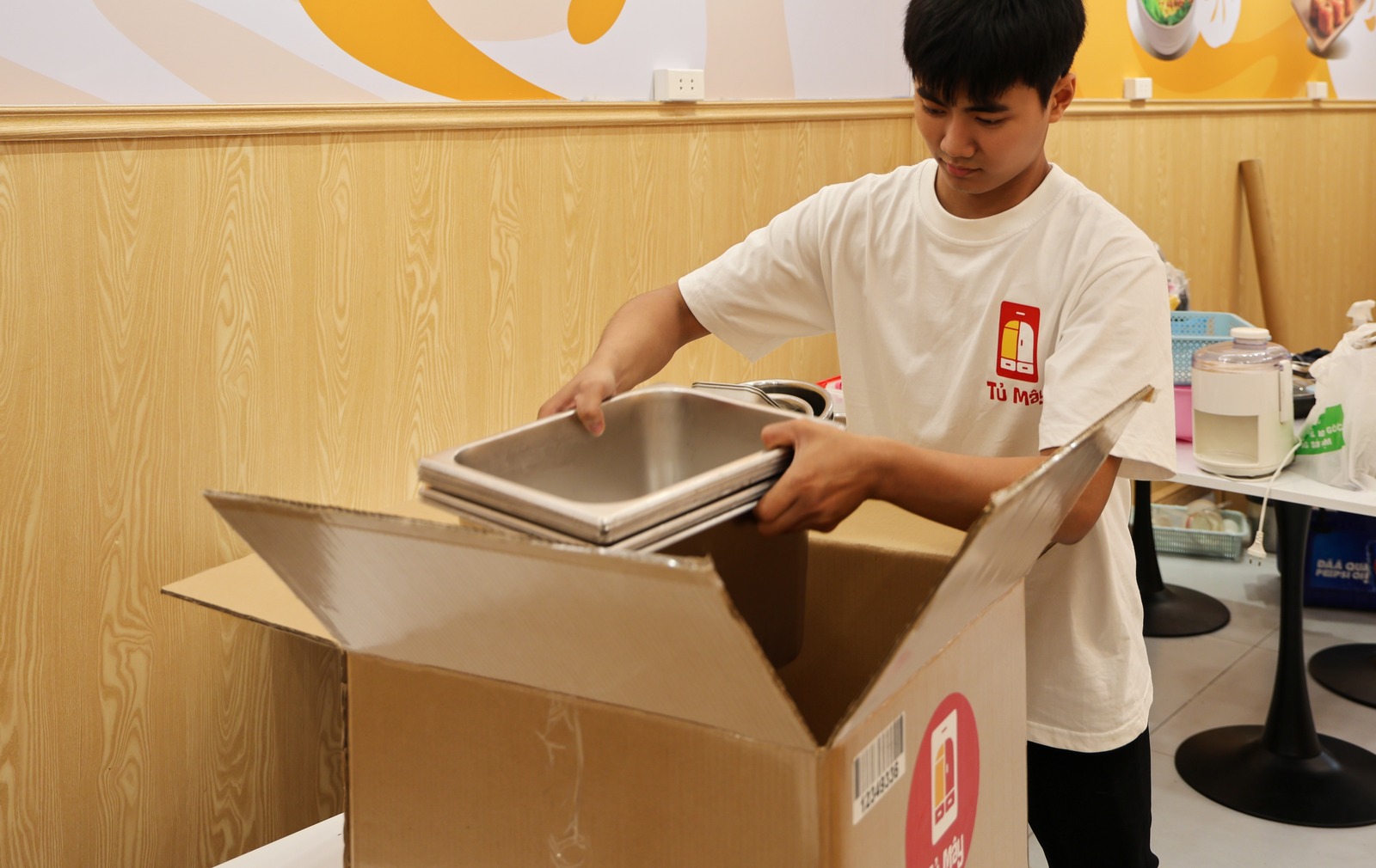 A crew member lowering a stack of steel pans into a Tủ Mây box