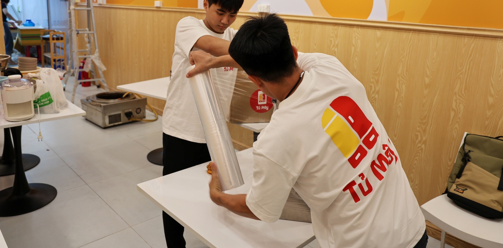 A crew member drawing stretch film around a kitchen machine on a table